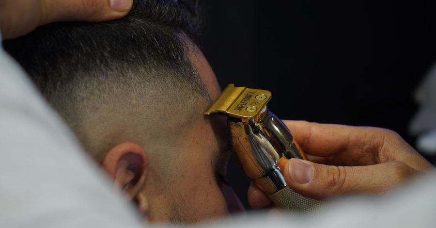 Per una barba sfumata in casa serve precisione, non fretta: Zoom su un barbiere che utilizza un rasoio elettrico per una…